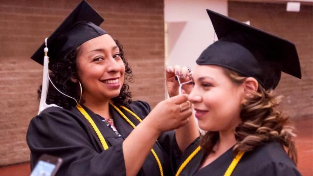 Grad helping another grad hang tassel on hat before commencement