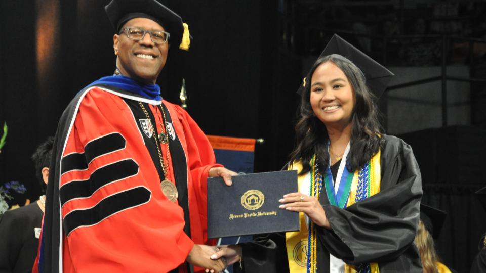 FPU President Andre Stephens presents a diploma to a graduate at the 2024 commencement