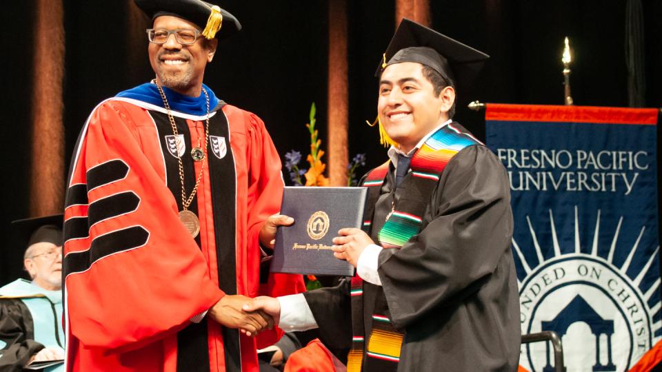 FPU President Andre Stephens presents a diploma to a graduate at the 2023 commencement
