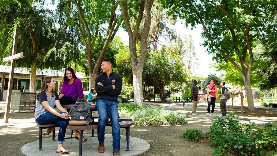 Two groups of students enjoy a sunny day in Alumni Plaza (The Forest) on the FPU main campus