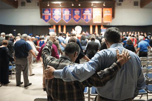 Adults joining hands and with arms around each other's shoulders pray at convoction