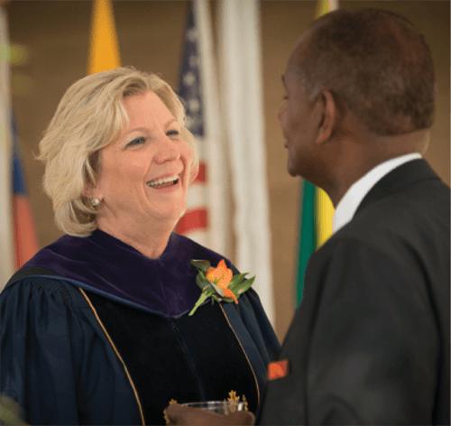 Dr. Jones shakes hands with a faculty member in regalia in front of world flags