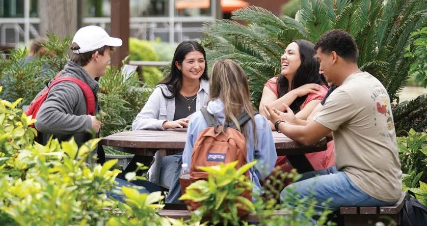A group of 5 students sitting and laughing in the Forest at FPU