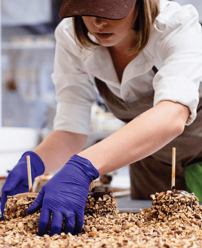 Stafford's Chocolates employee dipping chocolate apples in nuts