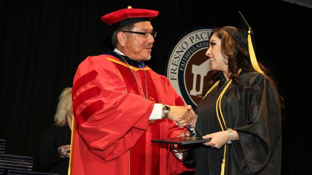 President Menjares shakes hand of FPU graduate receiving diploma