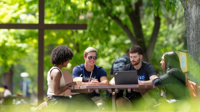 Students sitting outside around a table on campus with a cross in the background