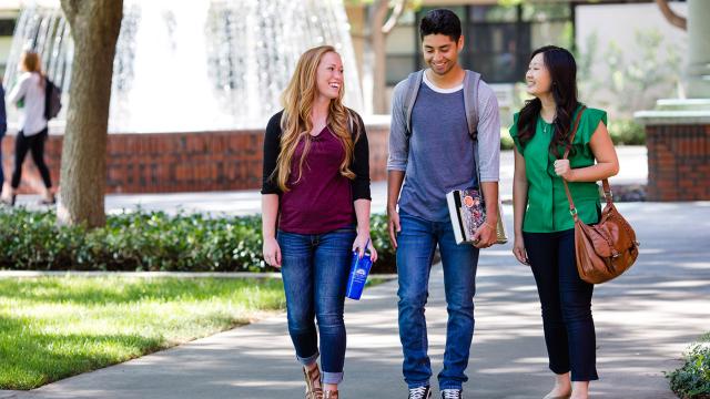 Three students walk by the McDonald Hall Fountain on the main FPU campus.