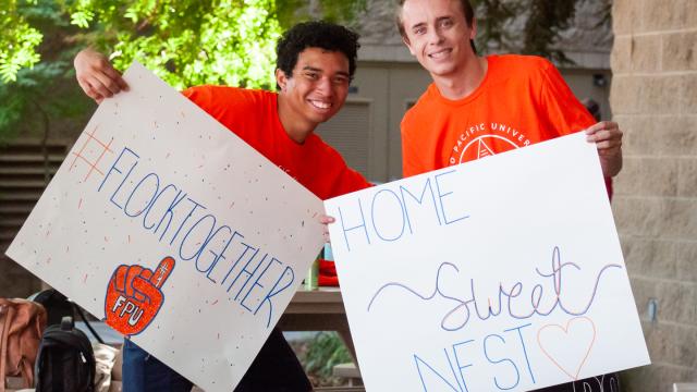 Two student volunteers smile and hold signs for new students arriving at Fresno Pacific University