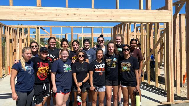 Members of the Sunbirds Women's Basketball Team pose in front of a house they are helping to build