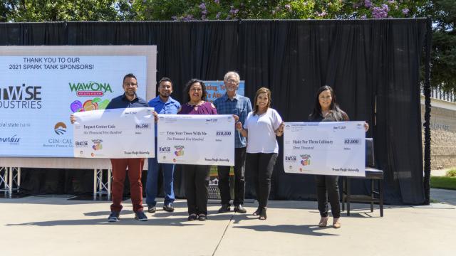 Three of the four Spark Tank winners stand with their big checks. From left: Impact Center Cafe, Trim a Tree with Me and Made for Them Culinary