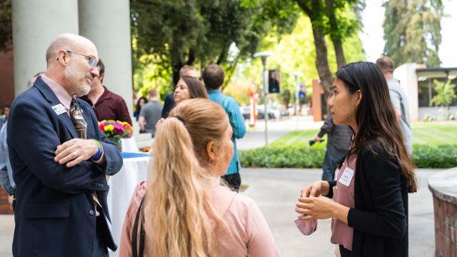 Marshall Johnston, Ph.D., associate professor of classics and ancient history, listens to honors student Veronica Mendez Garcia outdoors by the McDonald Hall Fountain at an event for Outstanding Graduates..